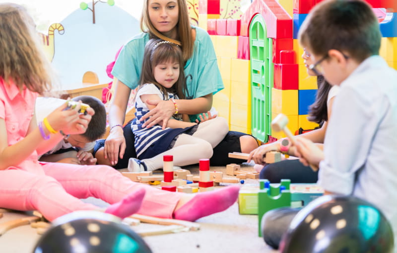 Kinder mit Betreuungsperson spielen auf einer Spieldecke